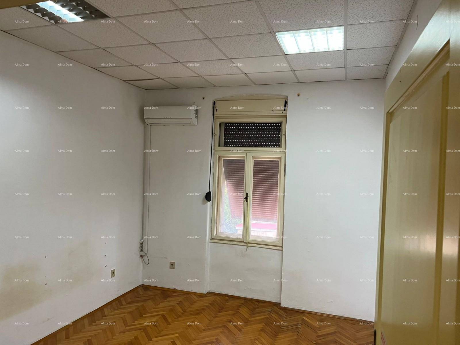 Helles Büro mit Fischgrätparkett, abgehängter Decke, Klimaanlage und einem Fenster mit Jalousien.