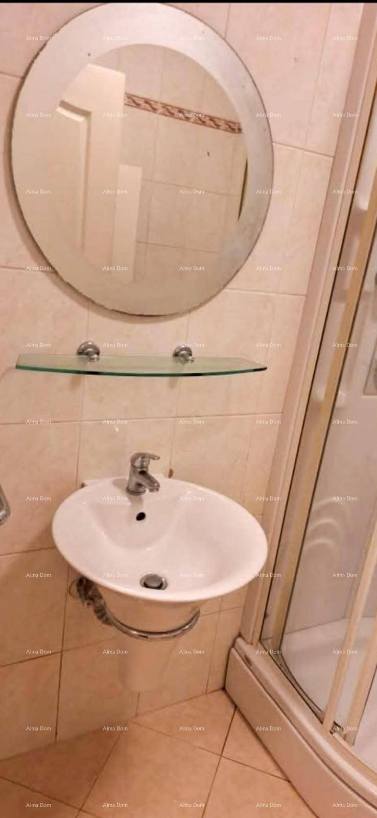 Badezimmer mit ovalem Spiegel über einem Waschbecken und einer Glasablage, Duschkabine teilweise sichtbar.