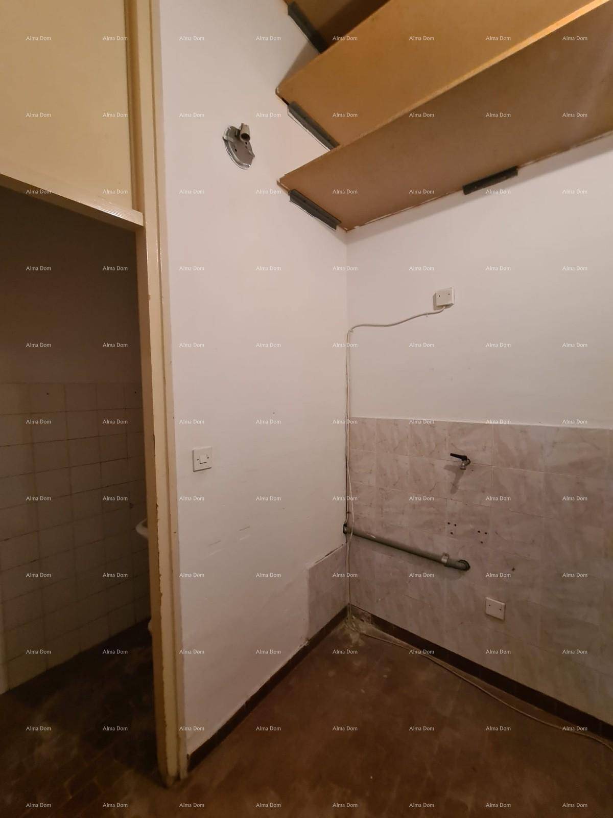 Raum mit gefliesten Wänden, sichtbaren Rohren und einem Holzboden, möglicherweise ein Badezimmer oder Hauswirtschaftsraum.