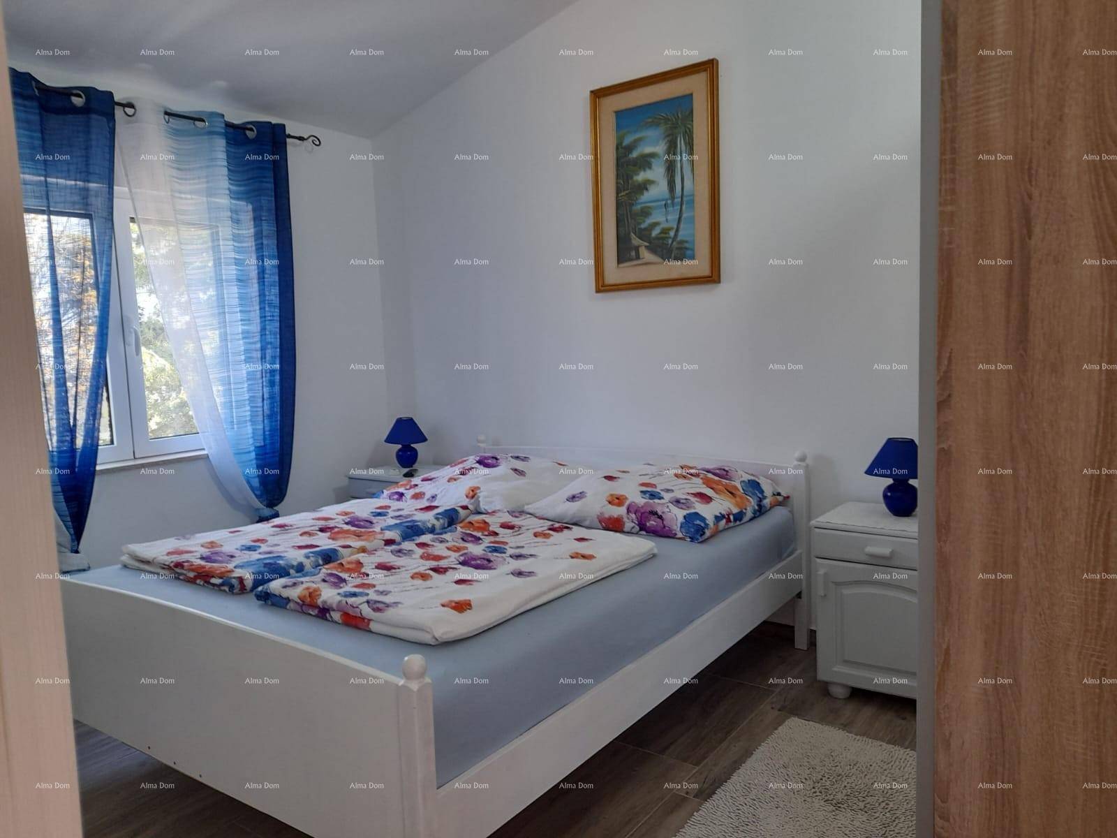 Helles Schlafzimmer mit Doppelbett, Nachttischen und einem Fenster mit blauen Vorhängen.