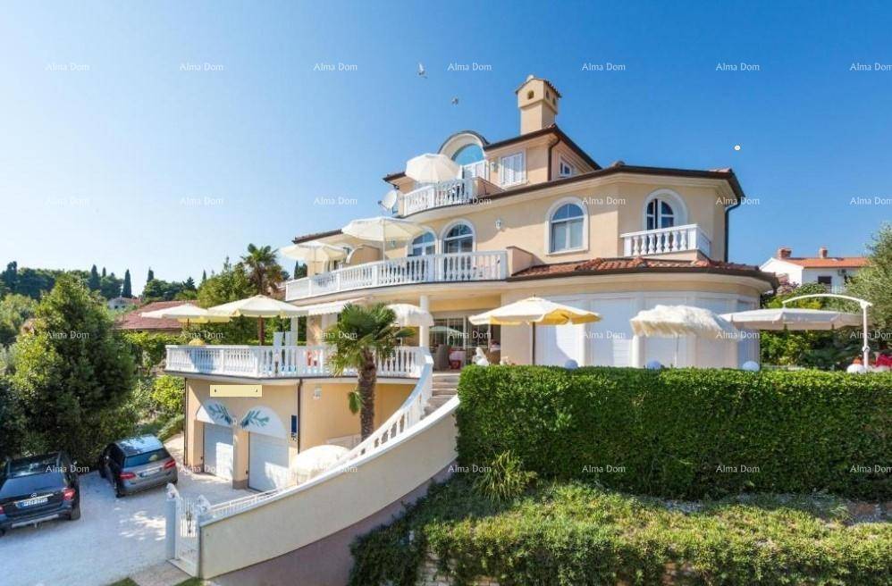 Ansicht der Villa von vorne mit mehreren Terrassen, Garagen und gepflegter Hecke.