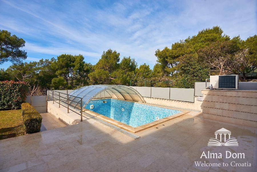 Großer Swimmingpool mit Mosaikfliesen und transparenter Überdachung, umgeben von einer Sonnenterrasse.