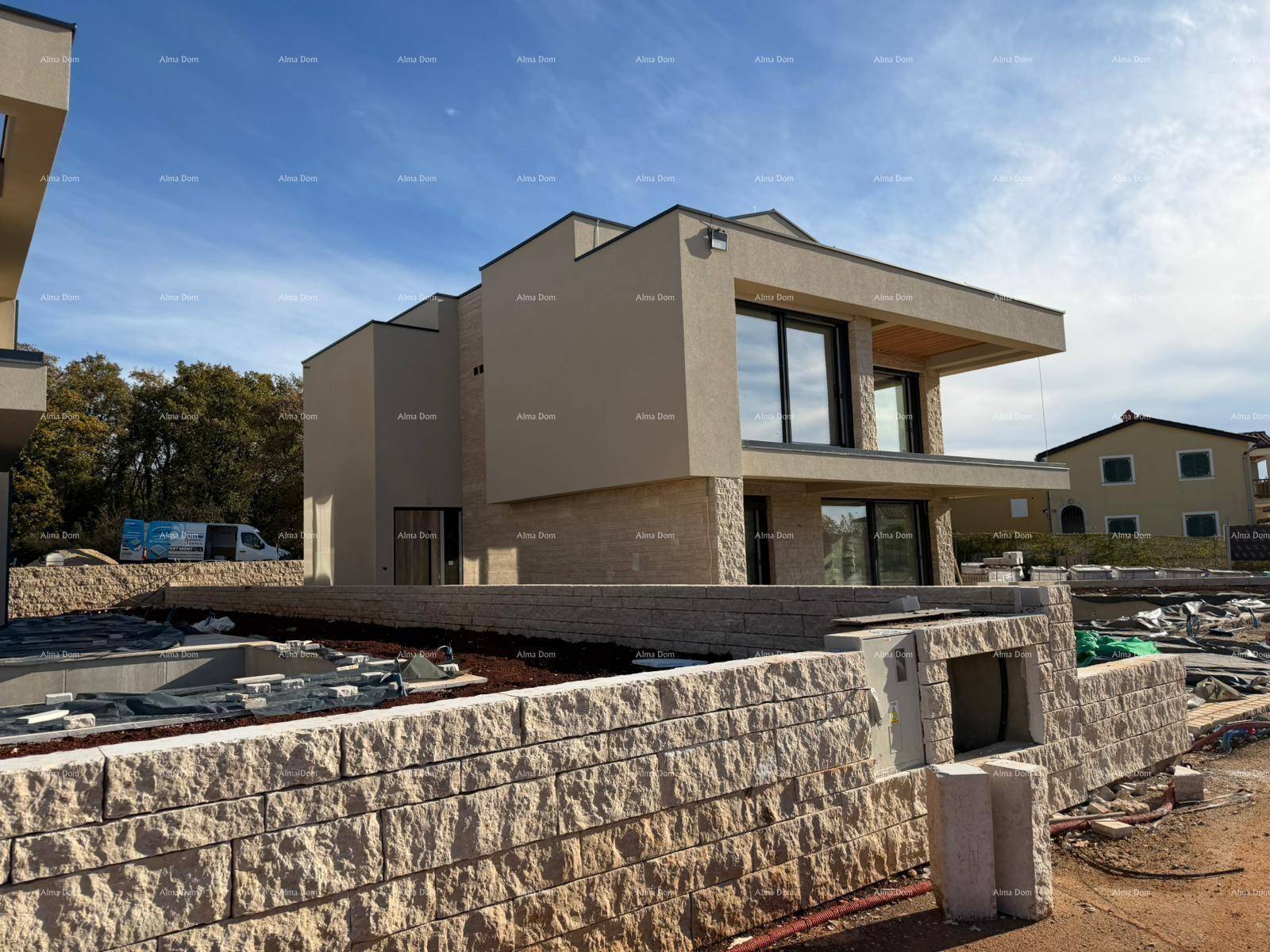 Seitenansicht einer modernen Villa im Bau mit Steinmauer und großen Fenstern.