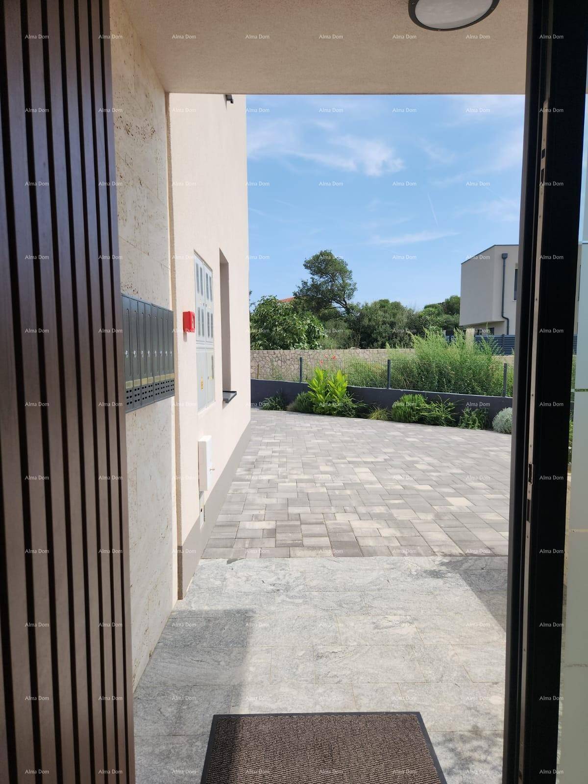 Eingangsbereich mit offener Tür und Blick auf den gepflasterten Vorplatz unter blauem Himmel.