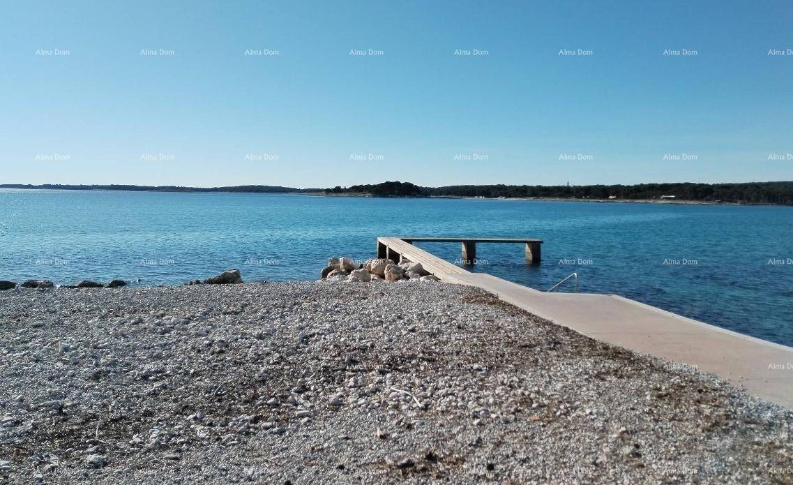 Ruhiges Meer mit einem kleinen Betonsteg und einem Kiesstrand im Vordergrund unter blauem Himmel.