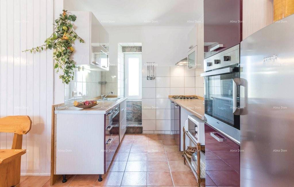 Schmale Küche mit weißen und lila Schränken, Fliesenboden und Fenster.