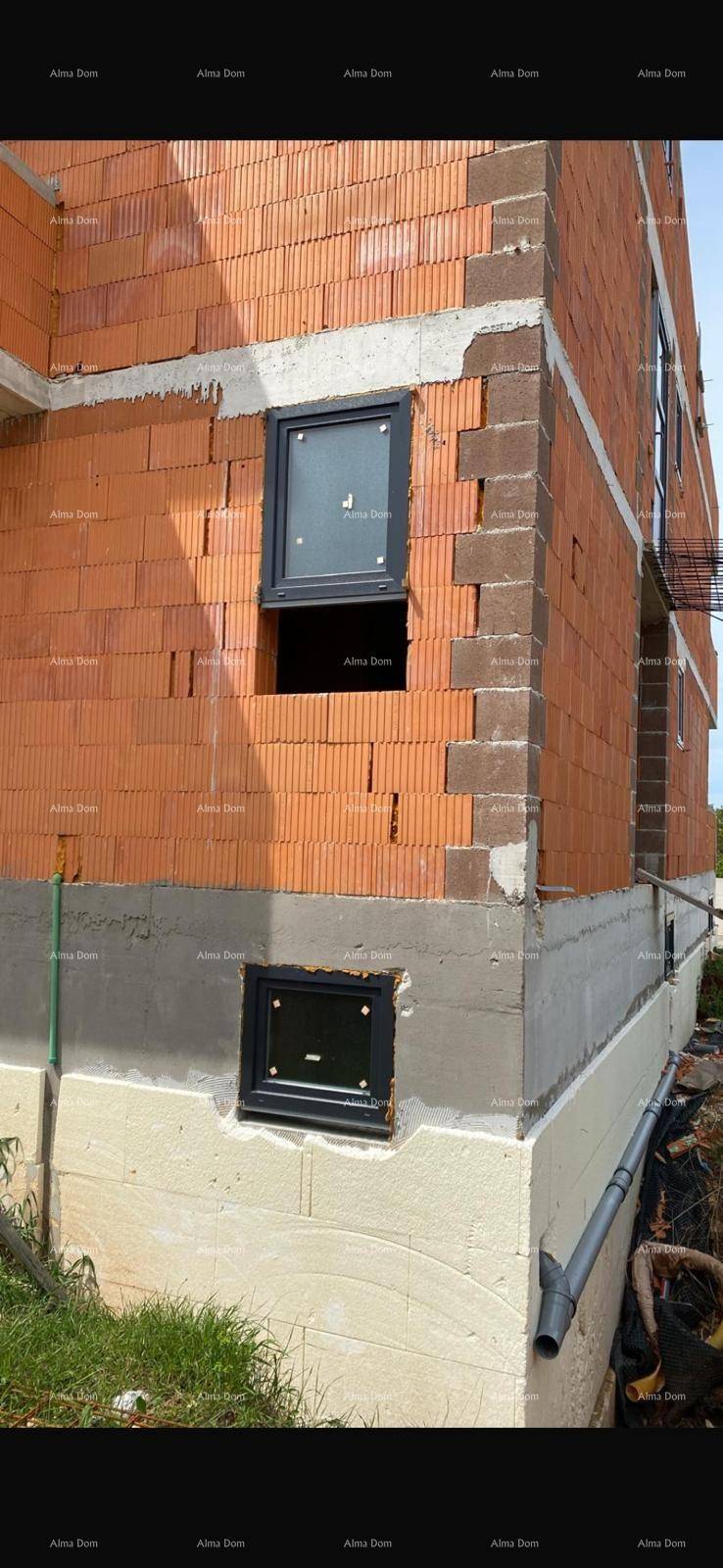 Detailansicht der Gebäudeecke im Rohbau mit roten Ziegeln und bereits eingesetzten dunklen Fenstern.