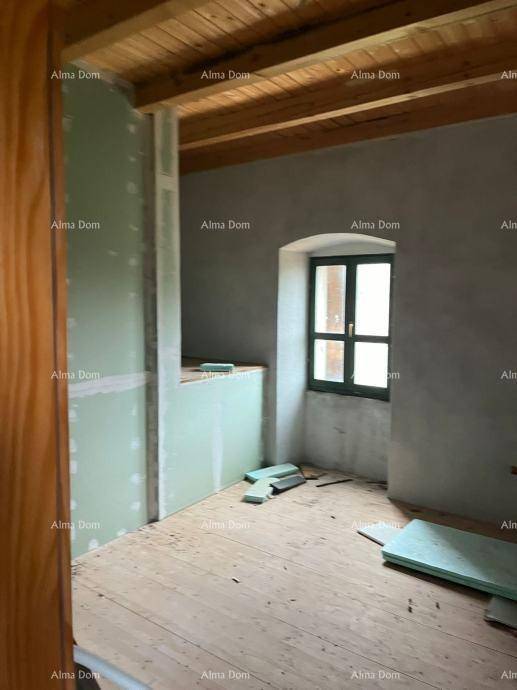 Innenraum im Rohbau mit Holzbalkendecke, Holzdielenboden und einem Fenster mit Rundbogen.