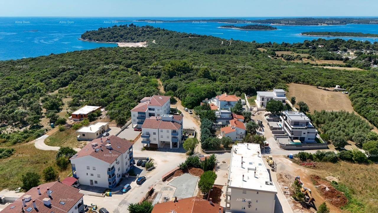 Weitläufige Luftaufnahme einer grünen Küstenregion mit vereinzelten Gebäuden und dem Meer.