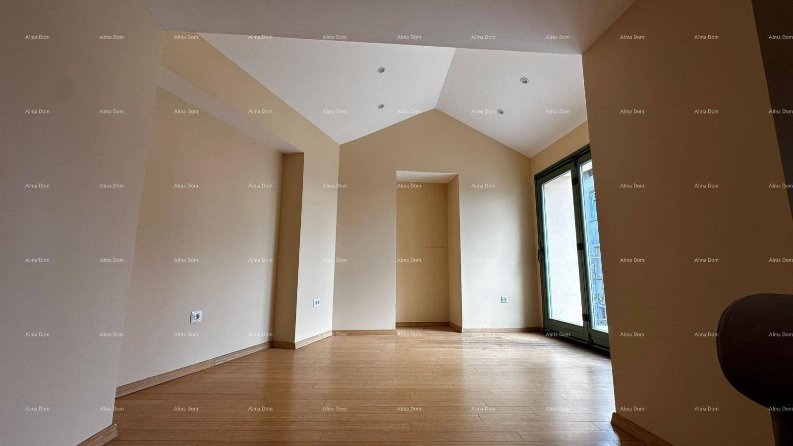 Heller, leerer Raum mit Holzboden, schräger Decke und großem Fenster mit Zugang nach draußen.