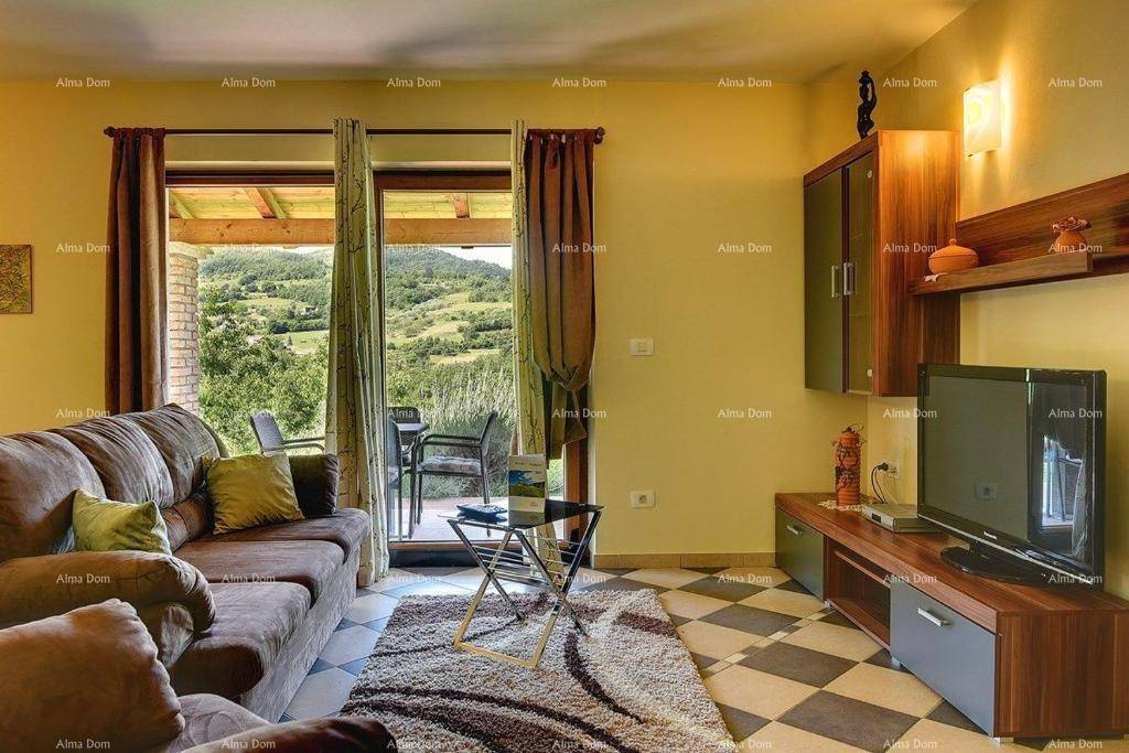Helles Wohnzimmer mit Sofa und Fernseher, großer Fensterfront und Zugang zur überdachten Terrasse mit Aussicht.