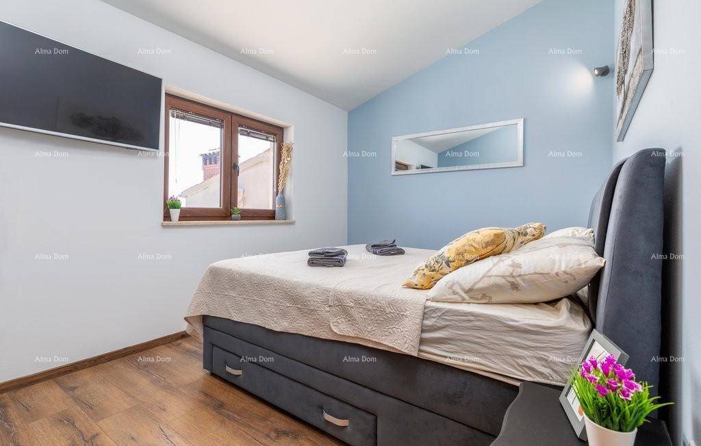 Helles Schlafzimmer mit Doppelbett, blauer Akzentwand, Holzboden und einem Fenster mit Blick nach draußen.