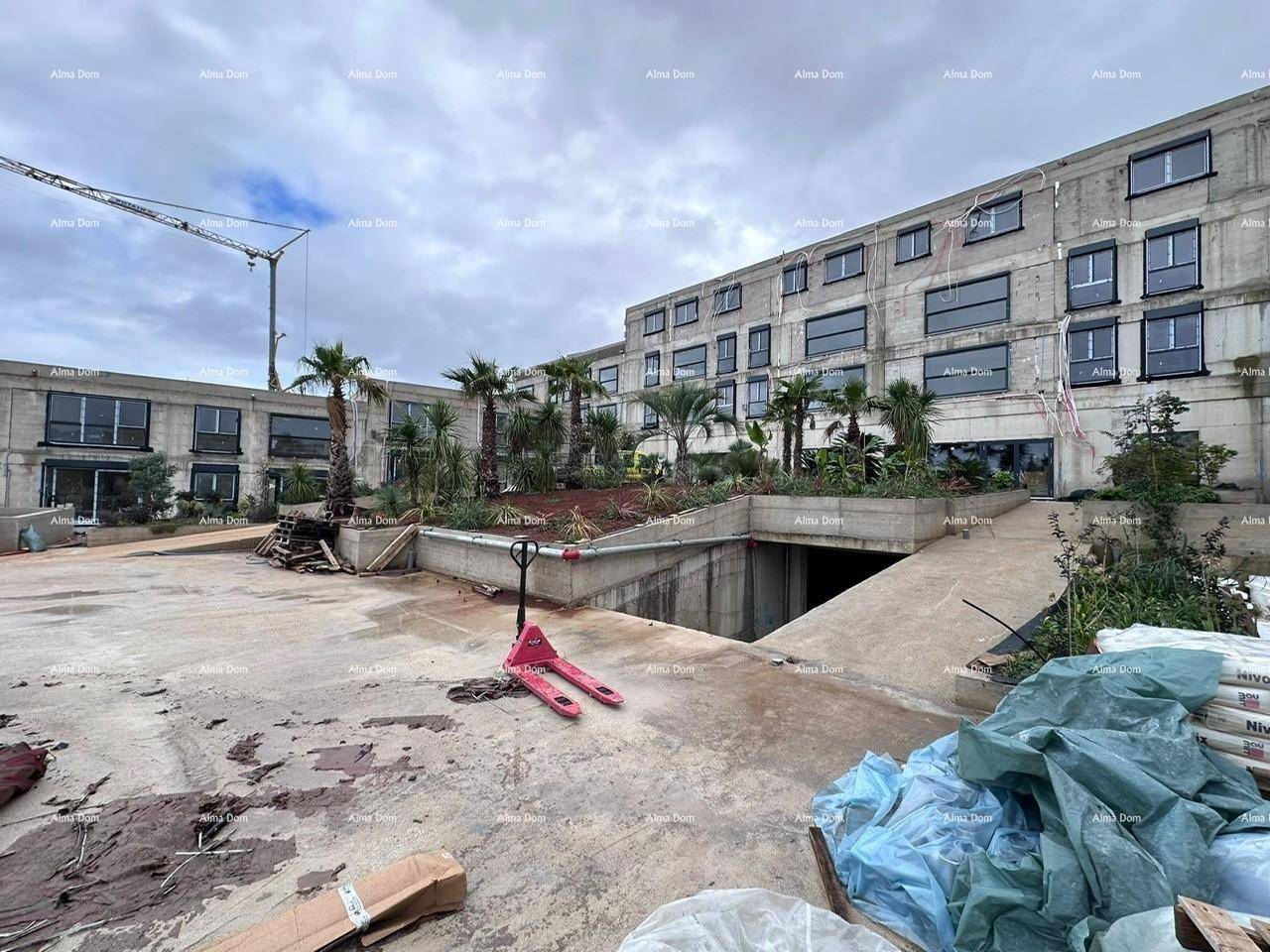 Baustelle mit Tiefgaragenzufahrt, Baugeräten und dem Rohbau eines modernen Gebäudes.
