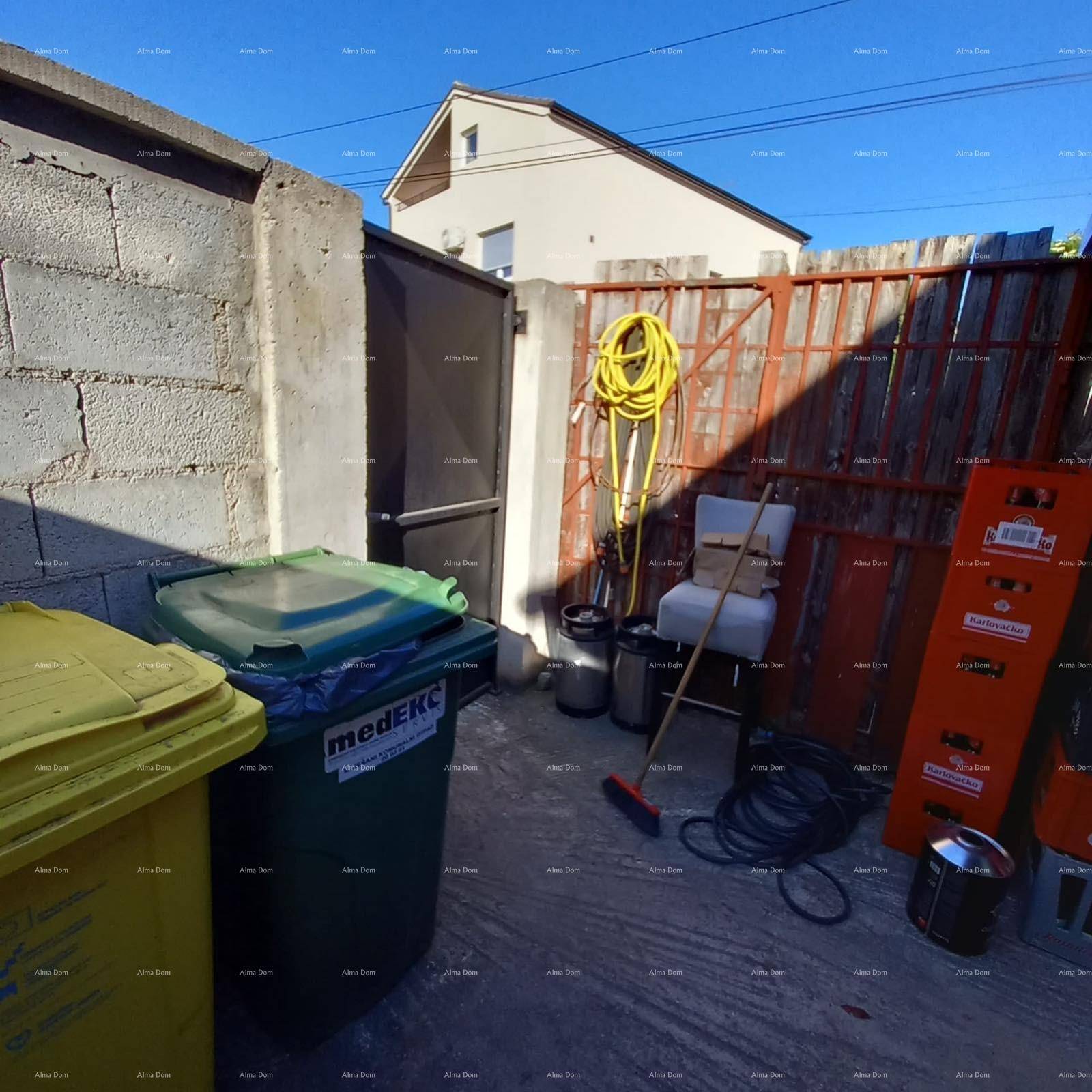 Hinterhofbereich mit Mülltonnen, Gartenschlauch und einem Zaun, neben einem Gebäude.