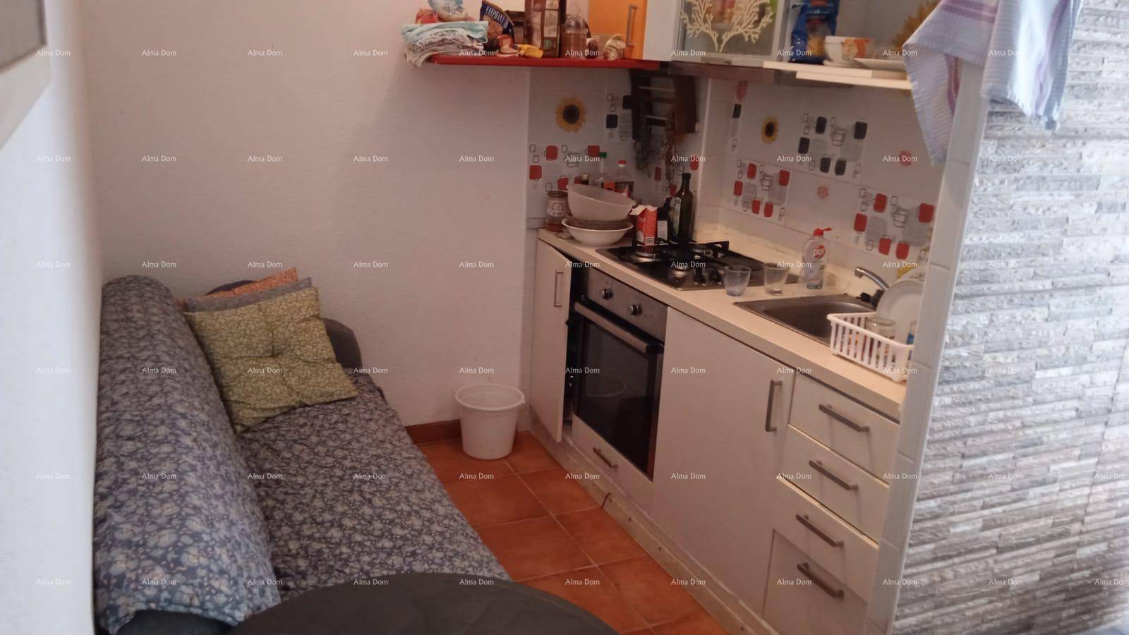 Kleine Küche mit Kochfeld, Backofen und angrenzendem Schlafsofa, ausgestattet mit Terrakottafliesen.