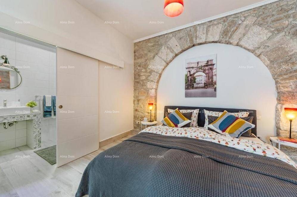 Schlafzimmer mit Doppelbett, Steinwand und direktem Zugang zu einem modernen Badezimmer.