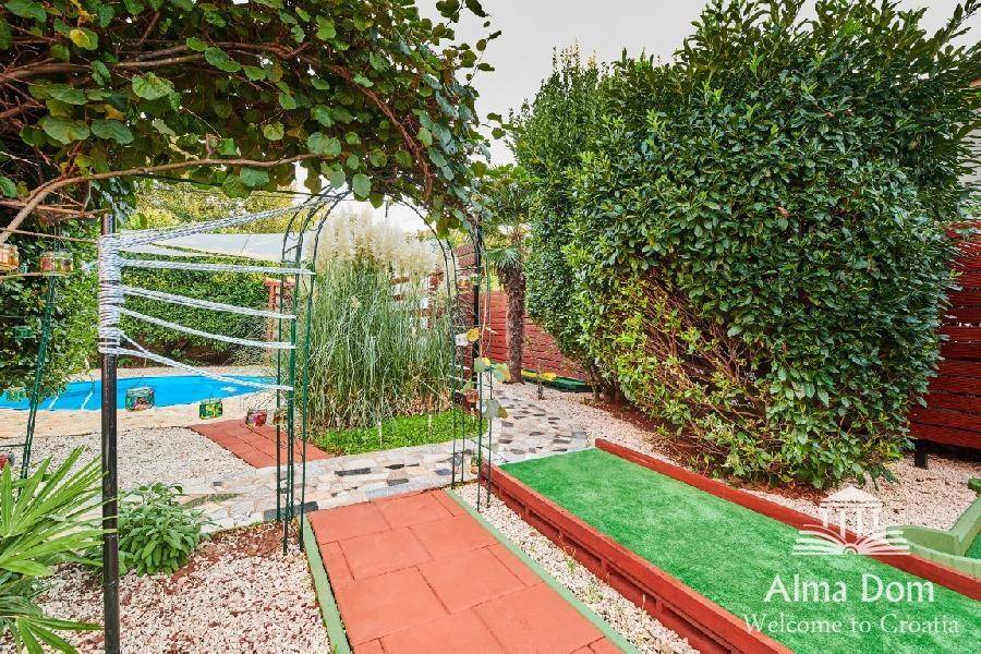Gartenweg mit Blick auf die Minigolfanlage und den Poolbereich in der Ferne.