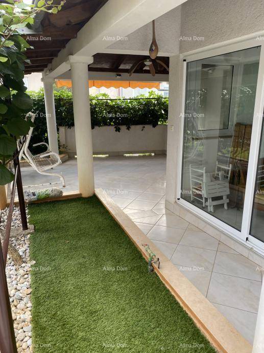 Überdachte Terrasse mit Fliesenboden, Kunstrasenstreifen und einer Schaukel im Freien.