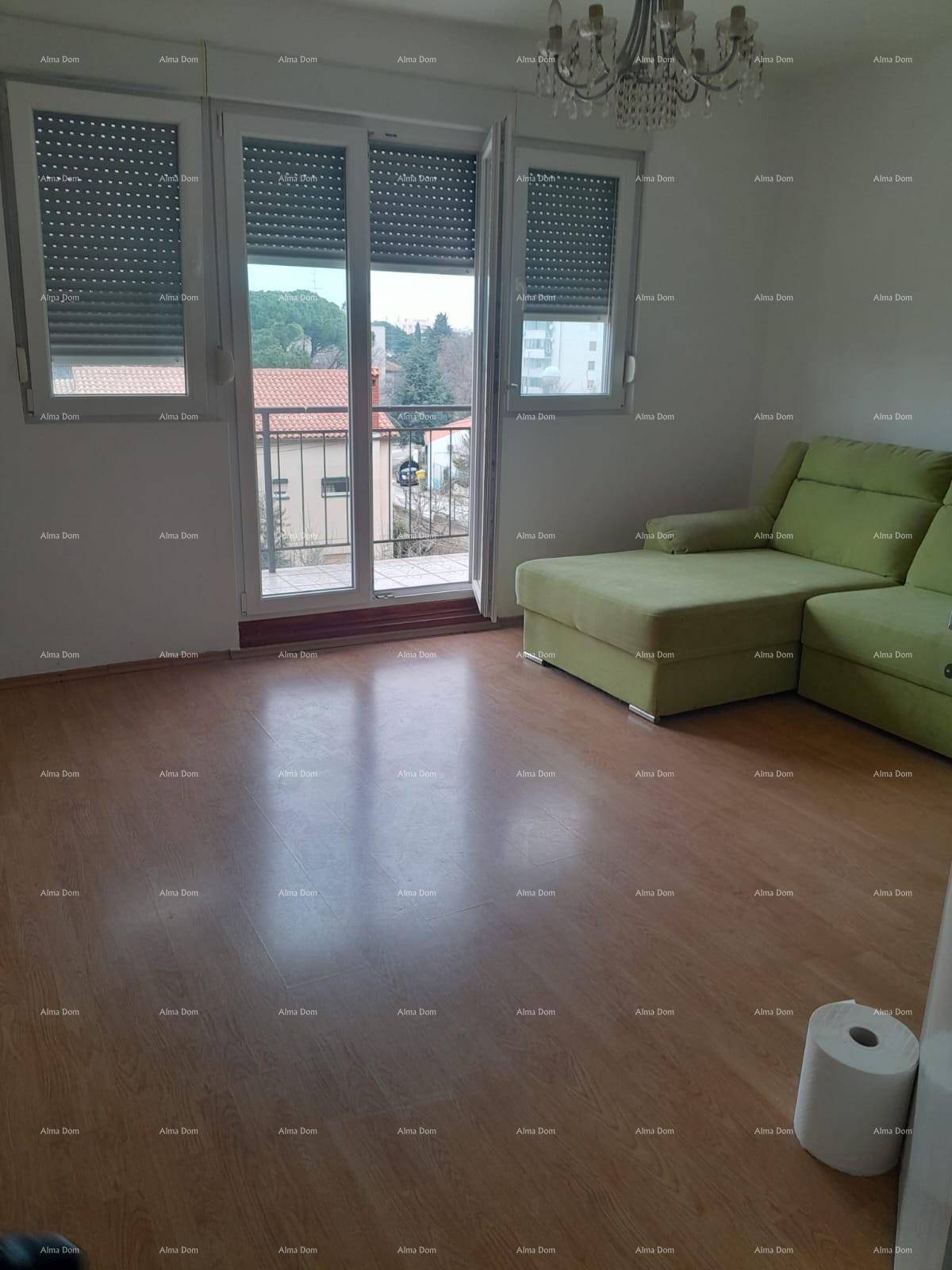 Wohnzimmer mit grünem Ecksofa, Laminatboden, Kronleuchter und Zugang zum Balkon.