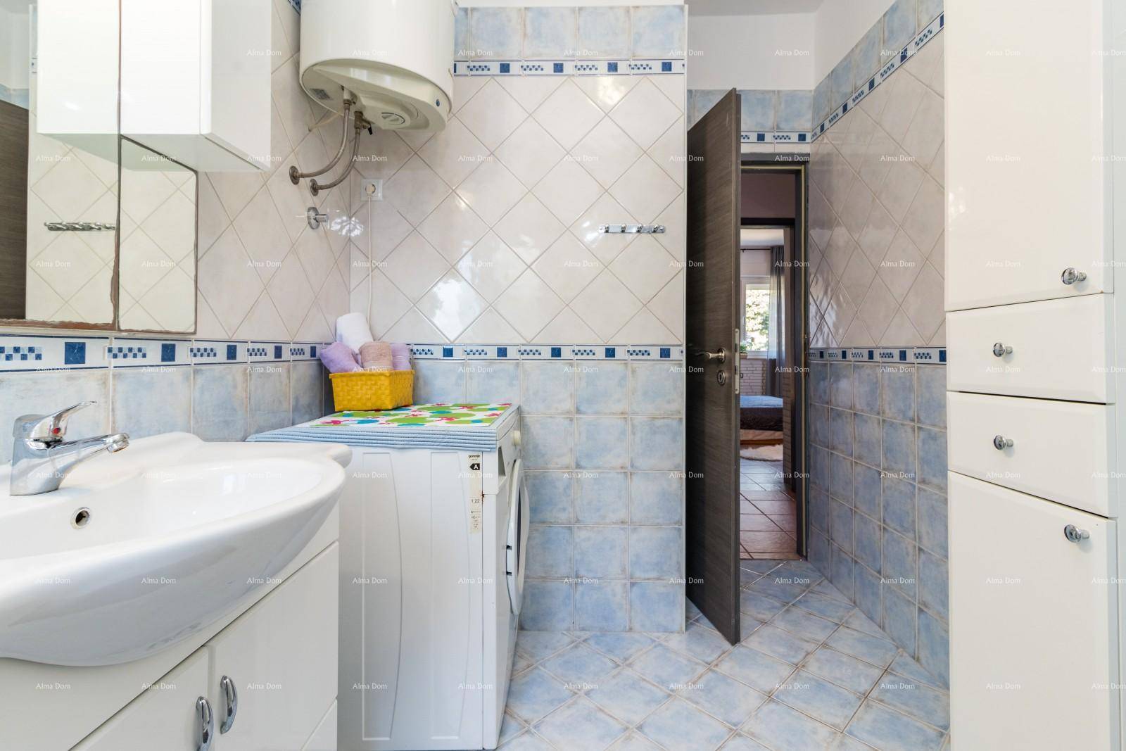 Badezimmer mit Waschmaschine, Waschbecken und blauen Fliesen, die einen Durchgang zeigen.