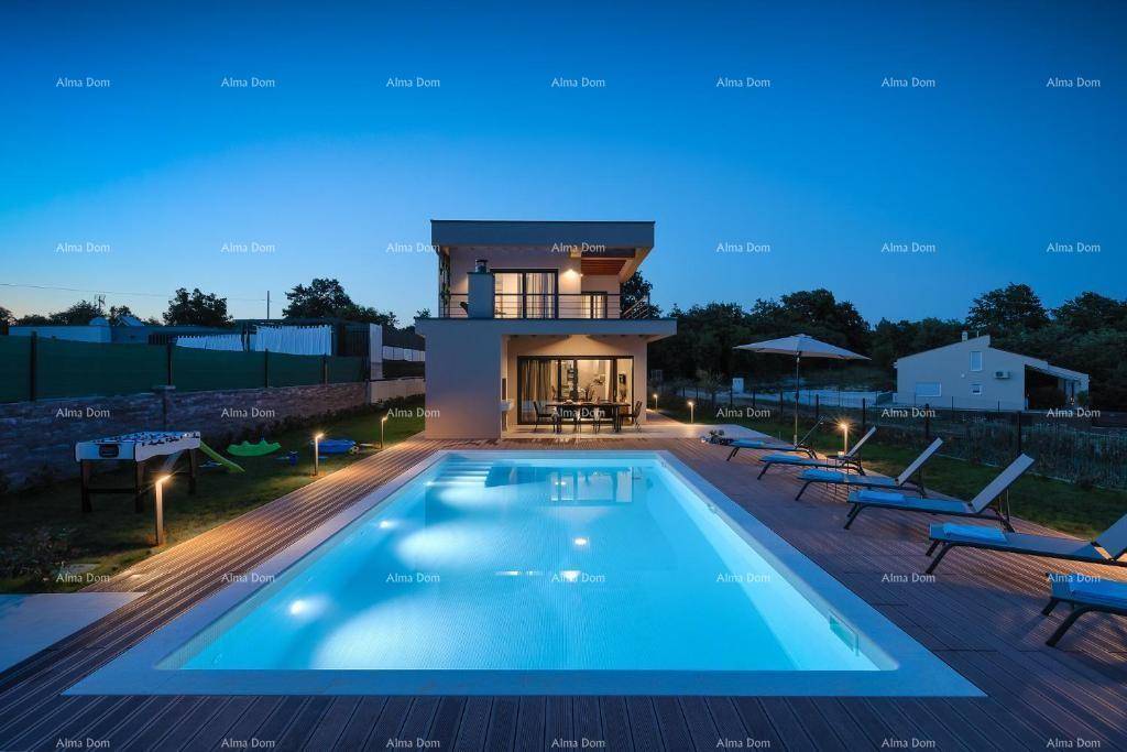 Weitläufige Außenansicht der Villa mit beleuchtetem Pool, Holzdeck und Garten bei Dämmerung.