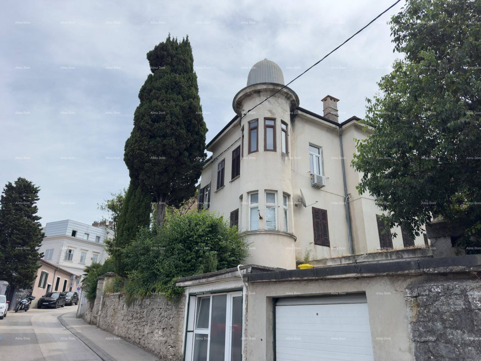Historisches Gebäude mit markantem Turm und Garage, aufgenommen an einem bewölkten Tag von der Straße.