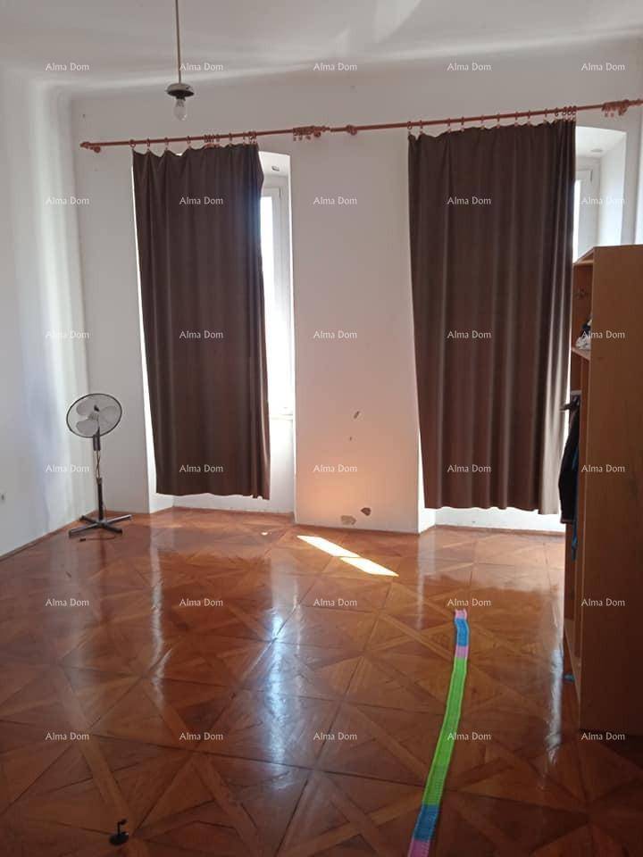 Geräumiger Raum mit glänzendem Parkettboden, zwei Fenstern und einem Ventilator, gut beleuchtet.