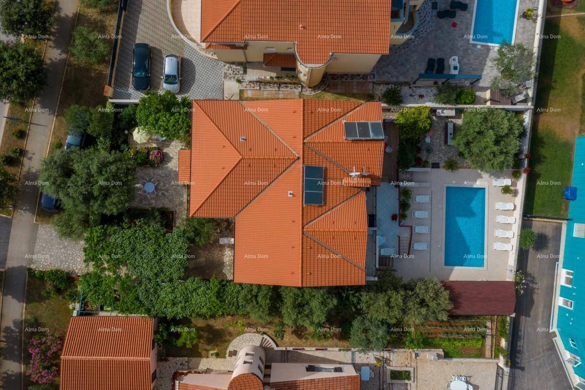 Luftaufnahme des Daches mit Ziegeln und Solarpaneelen, umgeben von grünen Bäumen und Gärten.