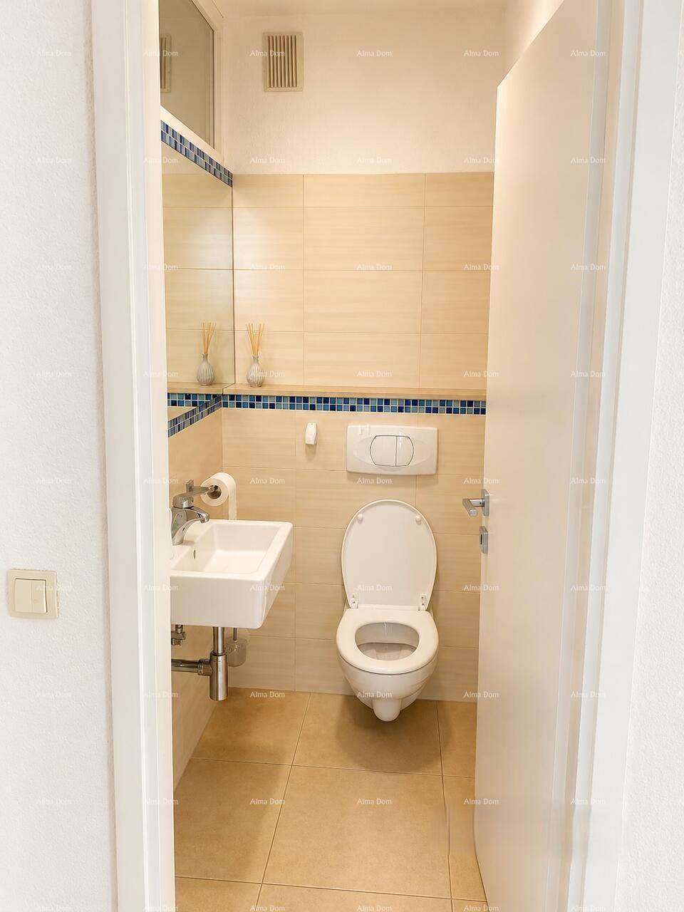 Kleines Gäste-WC mit beigefarbenen Fliesen, Wand-WC und Einzelwaschbecken, funktional und sauber.