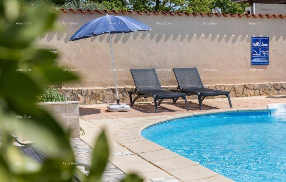 Blauer Swimmingpool mit Liegestühlen und Sonnenschirm, umgeben von einer Steinmauer.