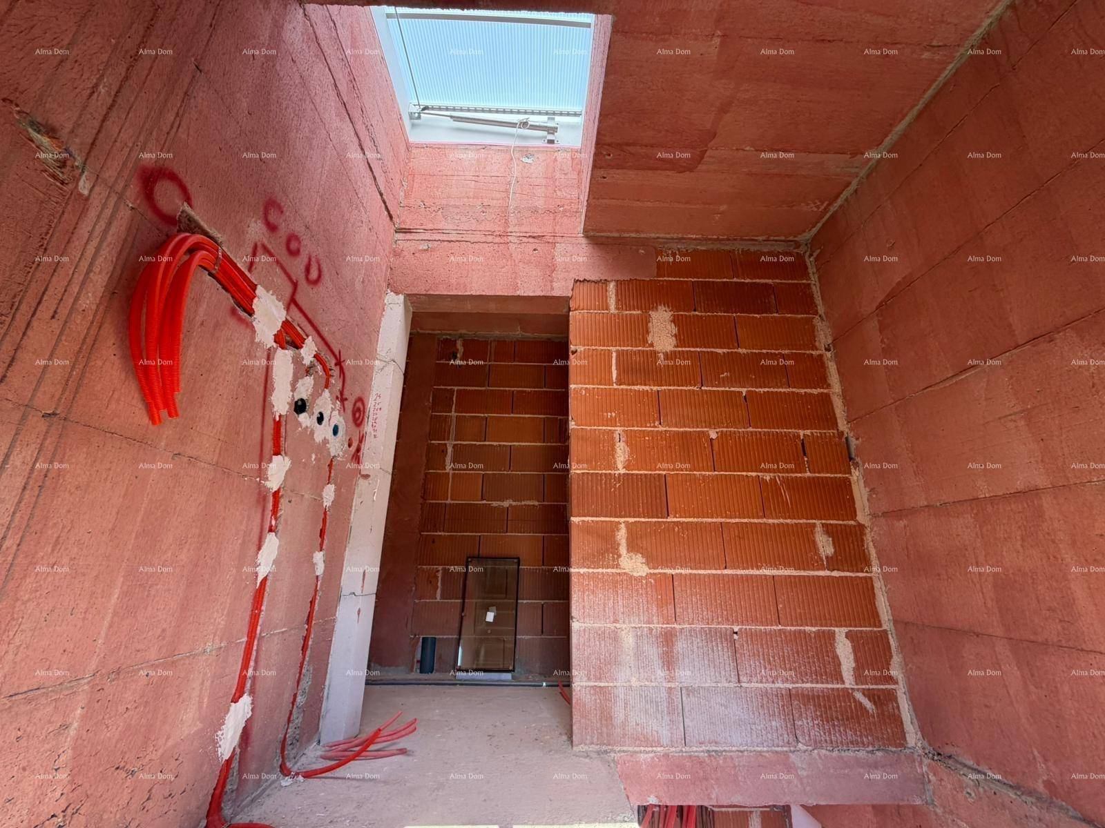 Ein Treppenhaus oder Flur im Rohbau mit sichtbaren Leitungen und einem Oberlicht für Helligkeit.