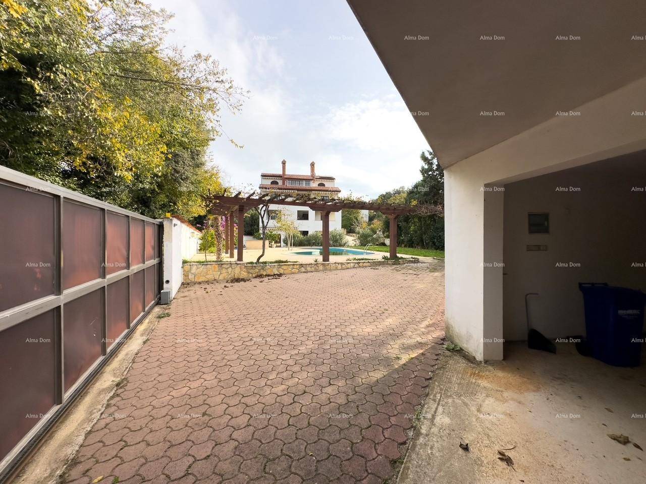 Blick vom Garagenbereich über die gepflasterte Zufahrt zum Hauptgebäude mit Pool im Hintergrund.