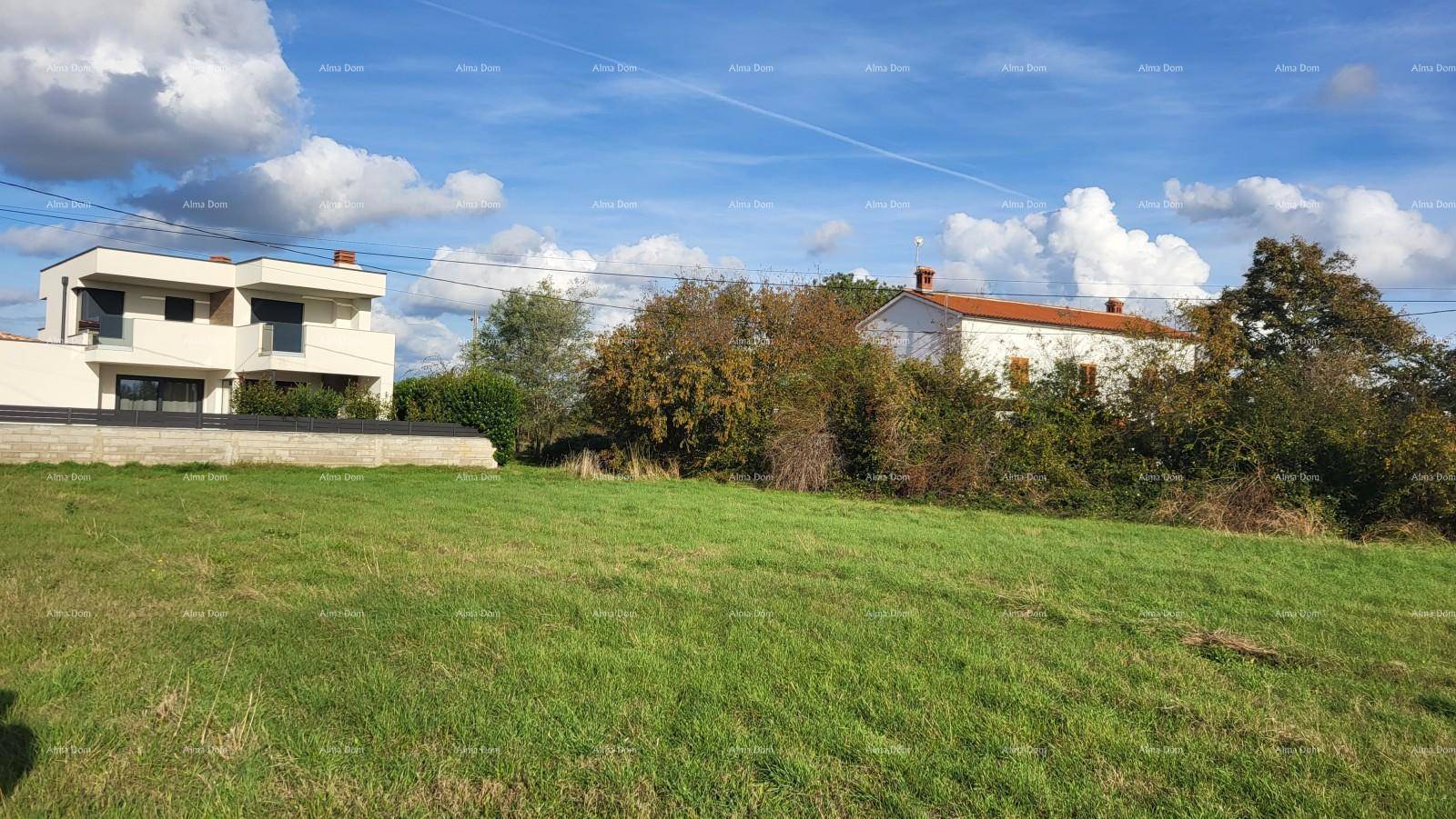 Offenes Feld mit saftigem Grün und Wohnhäusern in der Ferne unter einem teilweise bewölkten Himmel.