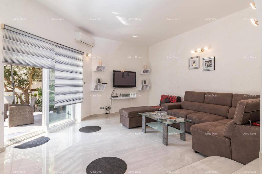 Helles Wohnzimmer mit bequemer Couch, Fernseher und Zugang zu einer Außenterrasse.