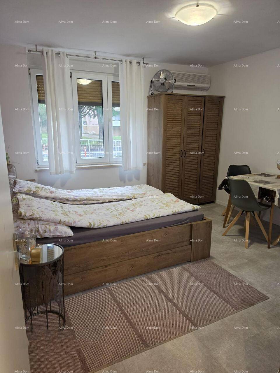 Helles Schlafzimmer mit Holzbett, Teppich und Fenster mit Blick nach draußen.