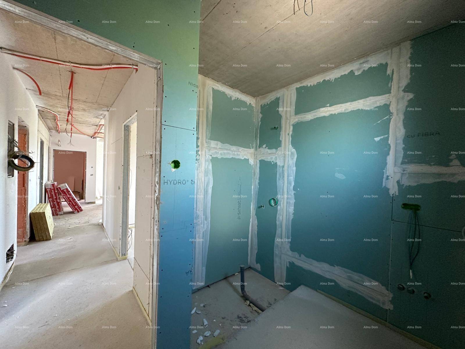 Innenräume im Rohbau mit Trockenbauwänden, sichtbaren Leitungen und einem Flur im Hintergrund.