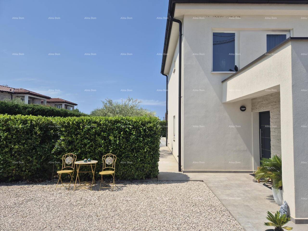 Seitlicher Eingangsbereich des Hauses mit Kiesfläche und einer kleinen Sitzgelegenheit im Grünen.