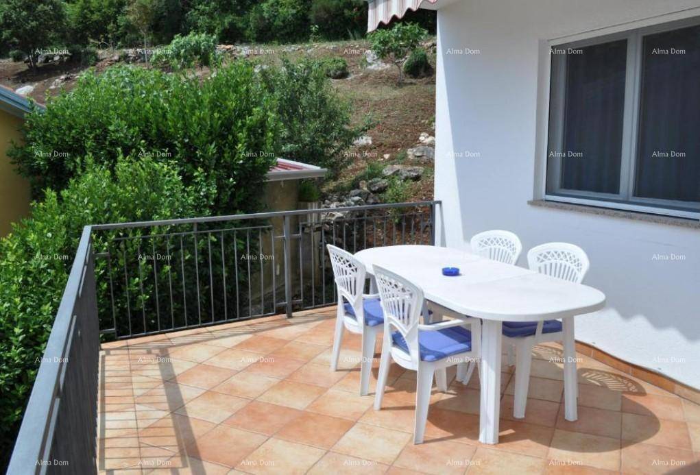 Balkon mit Fliesenboden, Esstisch und Stühlen, umgeben von grünen Büschen.