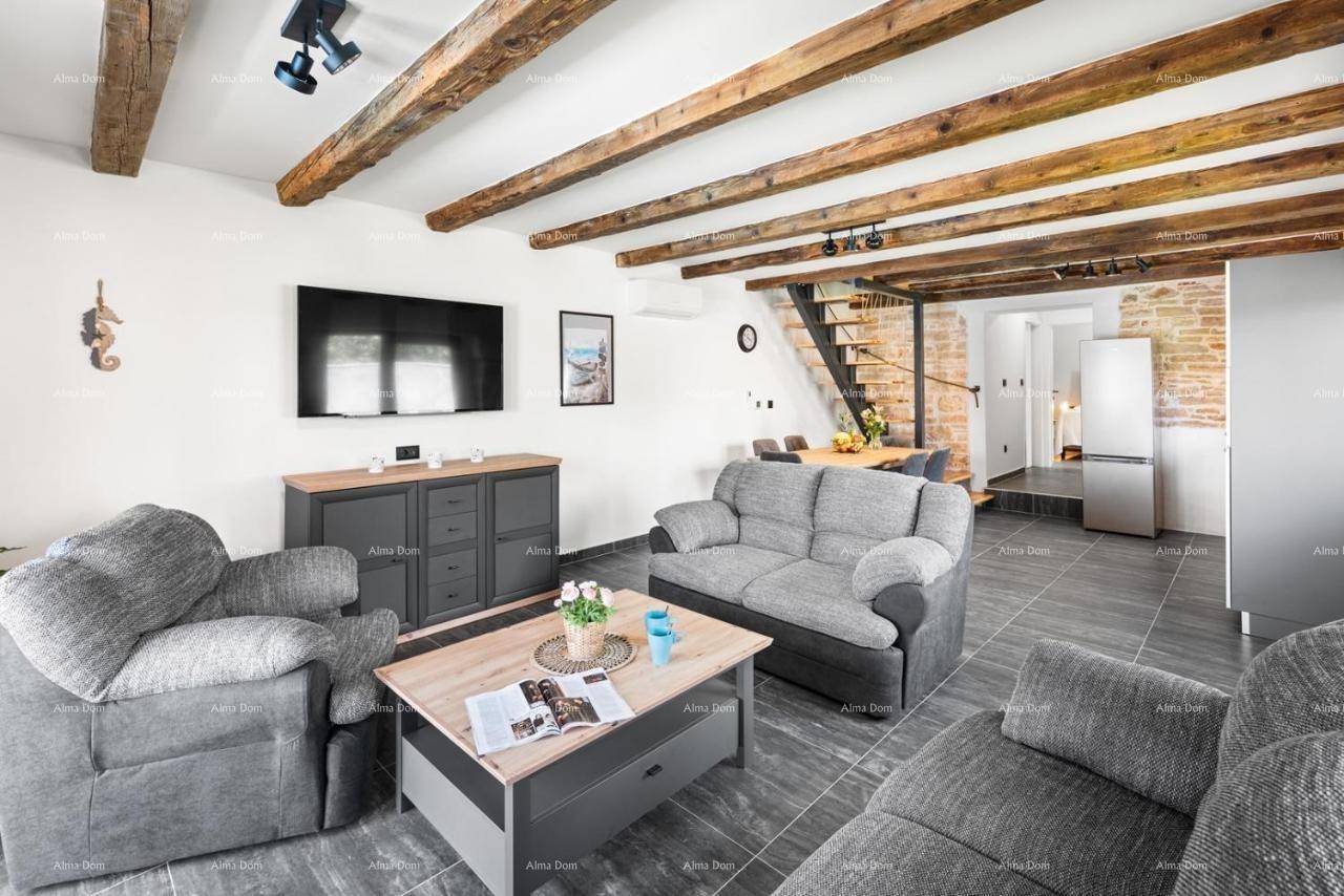 Heller Wohnbereich mit grauen Sofas, Holzbalken und einem modernen TV-Möbel, schafft eine einladende Atmosphäre.