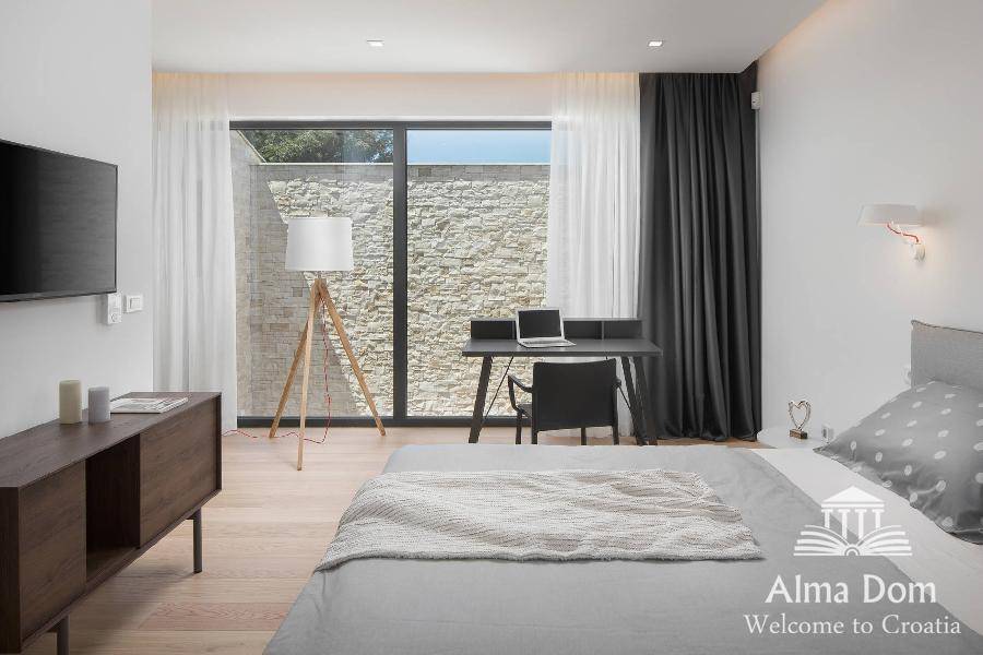 Modernes Schlafzimmer mit Arbeitsbereich, großem Fenster und Blick auf eine Steinmauer.
