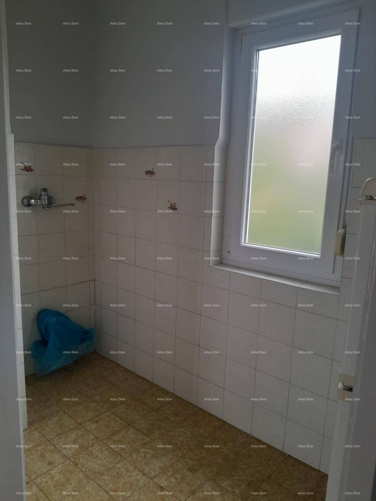Badezimmer mit weißen Wandfliesen, gemustertem Fliesenboden und einem Fenster für Tageslicht.