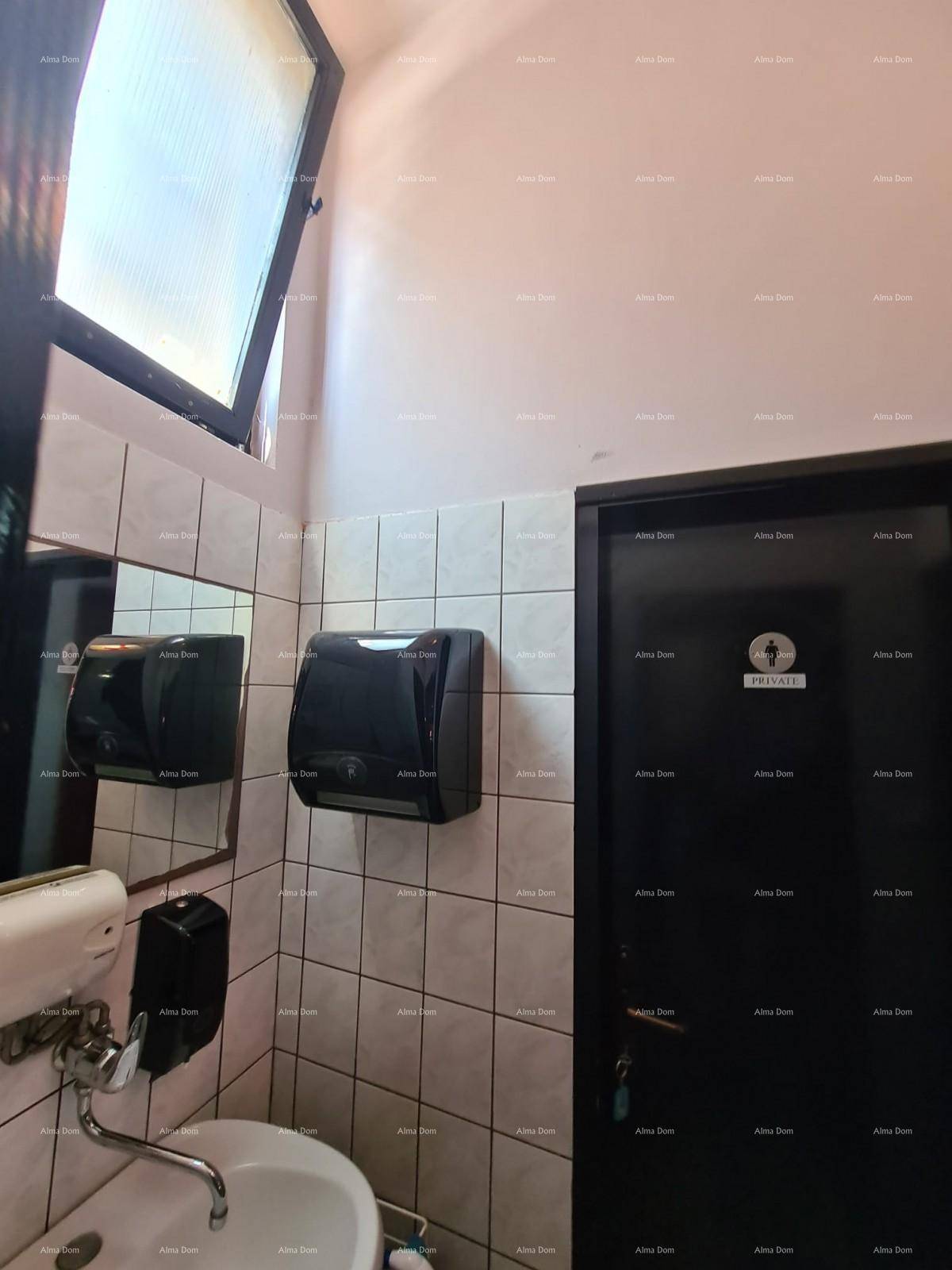 Waschbereich in einer Toilette mit Waschbecken, Spiegel und einem Handtuchspender an der gefliesten Wand.