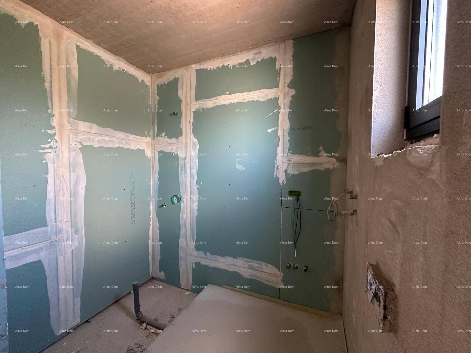 Badezimmer im Rohbau mit Trockenbauwänden, sichtbaren Installationen und einem Fenster für Tageslicht.