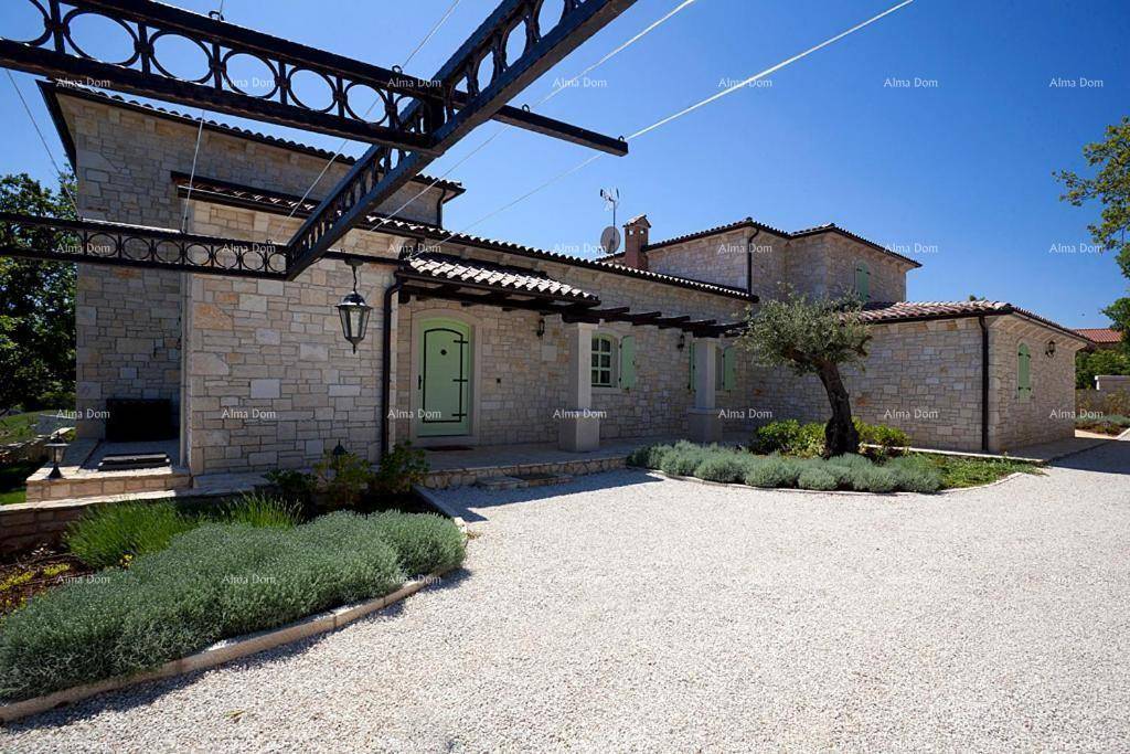Ansicht der Steinvilla mit markanter Pergola und gepflegtem Vorgarten unter blauem Himmel.