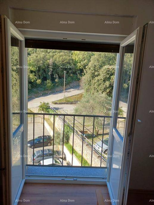 Blick aus einem geöffneten Fenster auf die darunterliegende Straße mit parkenden Autos und grünen Bäumen.