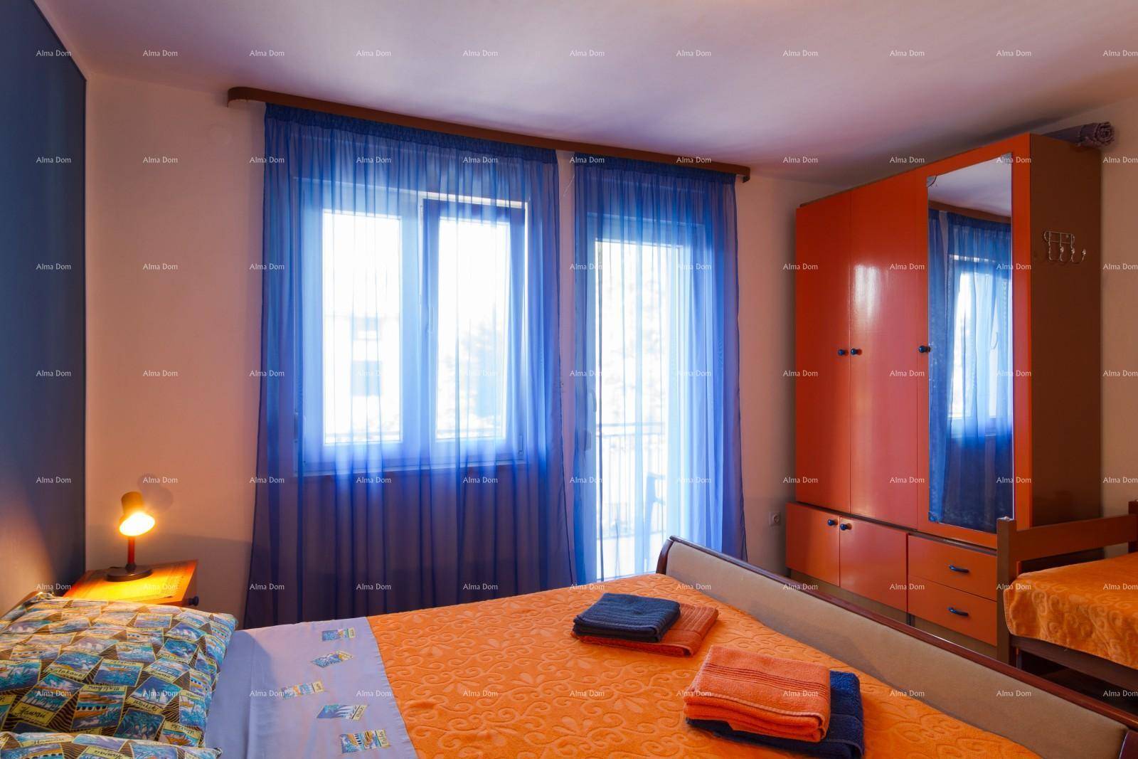 Schlafzimmer mit blauer Wand, orangefarbenem Kleiderschrank und Bett, sowie hellen Vorhängen.