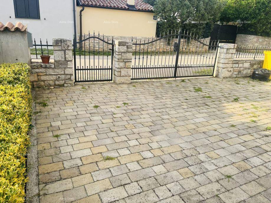 Einfahrt mit schmiedeeisernem Tor und gepflastertem Bereich, umgeben von einer niedrigen Hecke.