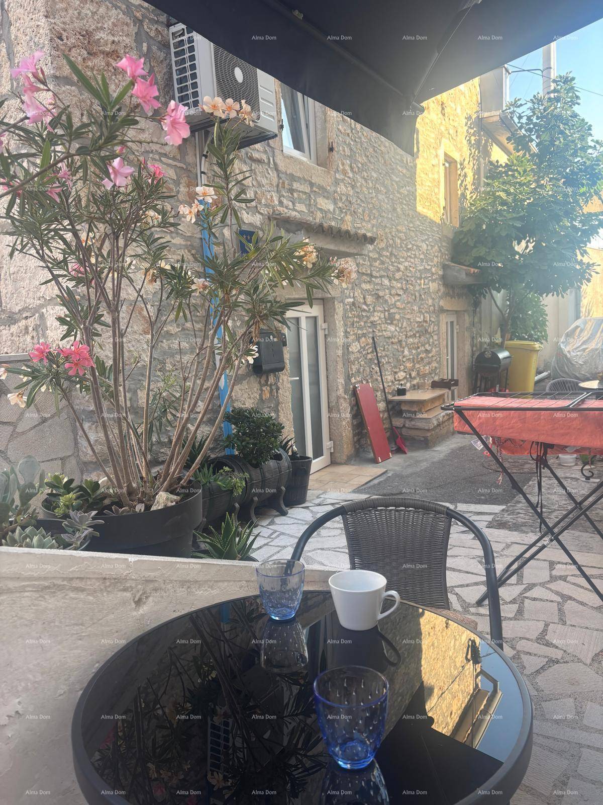 Gemütlicher Außenbereich mit Steinfassade, Tisch und Stühlen unter einem Sonnenschirm.