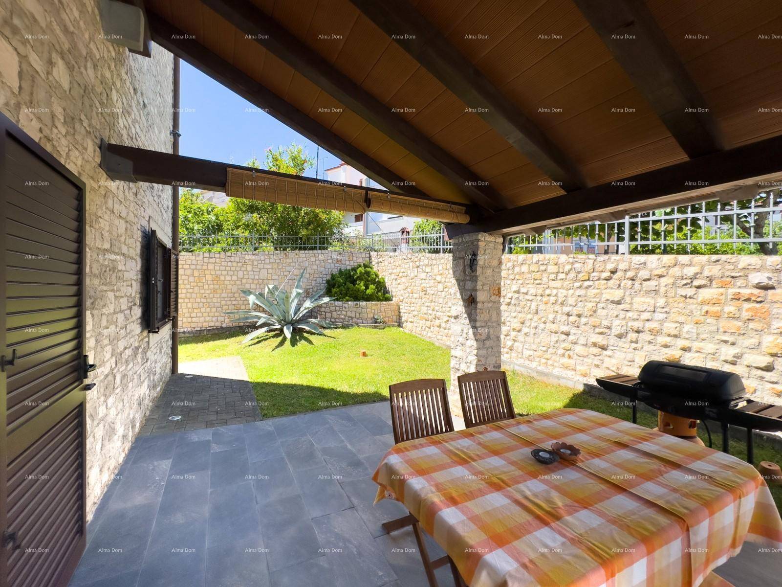 Überdachte Terrasse mit Esstisch und Grillbereich, umgeben von Steinmauern und Grünfläche.