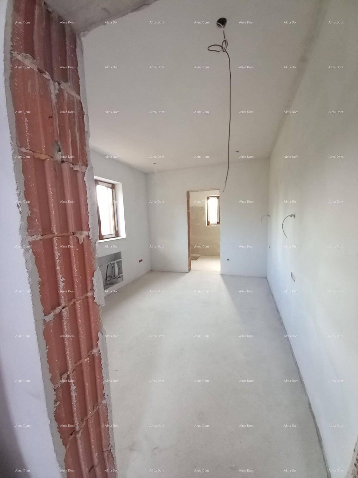 Flur im Rohbau mit sichtbaren Ziegelwänden und Fenstern.